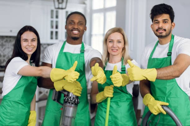 Diverse professional cleaning team in green aprons and yellow gloves giving a thumbs up.