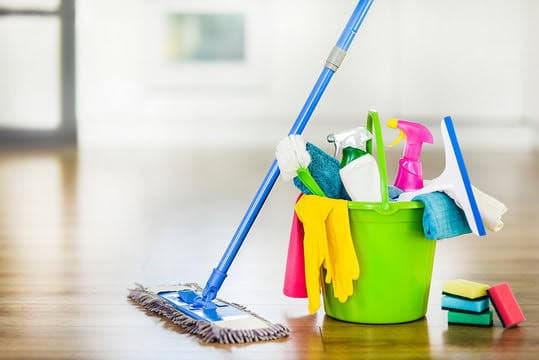 A blue mop and green bucket filled with cleaning supplies on a bright wooden floor.