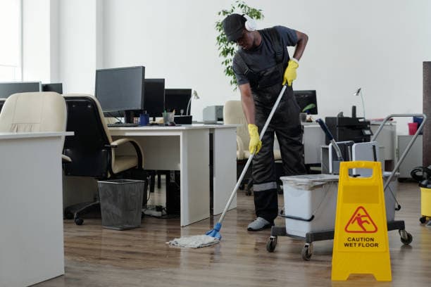 Professional cleaner mopping an office floor with a yellow caution sign in the foreground.