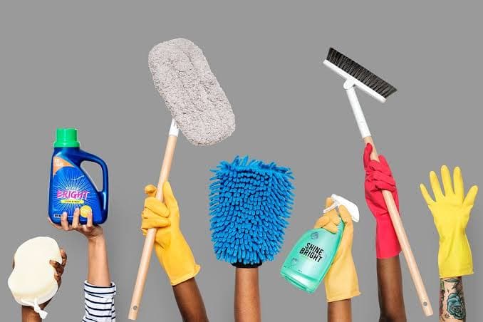 Hands in colorful gloves holding cleaning supplies like a mop, brush, and spray bottles.